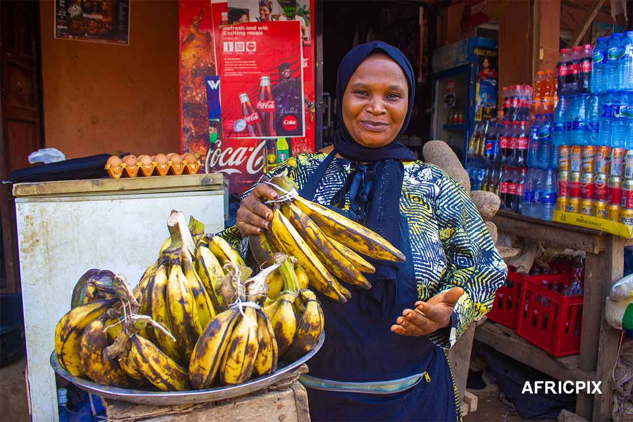 Nigeria Market Woman In Front of Shop Holding Banana